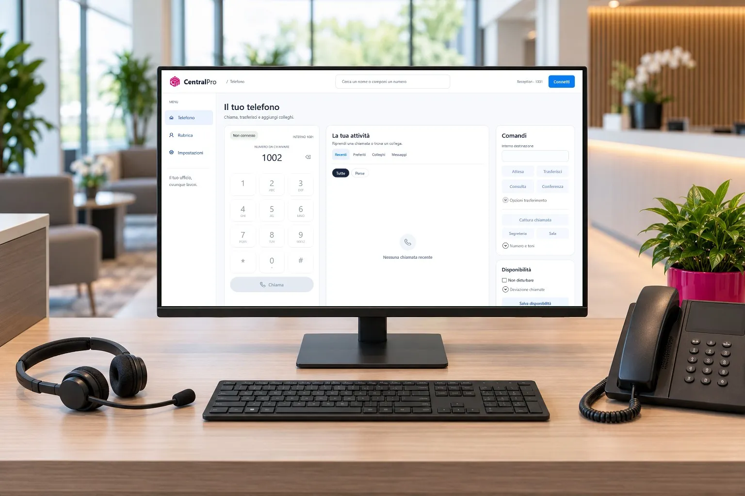 Il telefono di CentralPro aperto sul monitor di una reception, accanto a un telefono da scrivania e a una cuffia